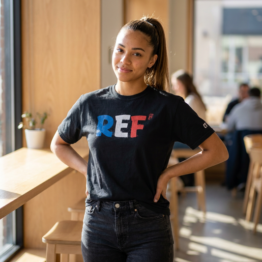 Woman wearing the black Ref' Crew Tricolore Tee in a sunlit café – blue, white and red REF' print across the chest