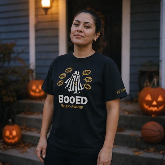 Woman wearing the black Booed Year-Round Tee on porch steps lined with jack-o'-lanterns and a basketball at dusk – Ref' Crew basketball referee Halloween tee
