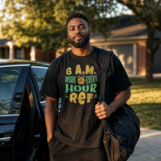 Basketball referee in the morning light, gym bag over the shoulder, wearing the black Ref' Crew 8 A.M. tee — retro gold and mint lettering reading 8 A.M. WORK EVERY HOUR REF
