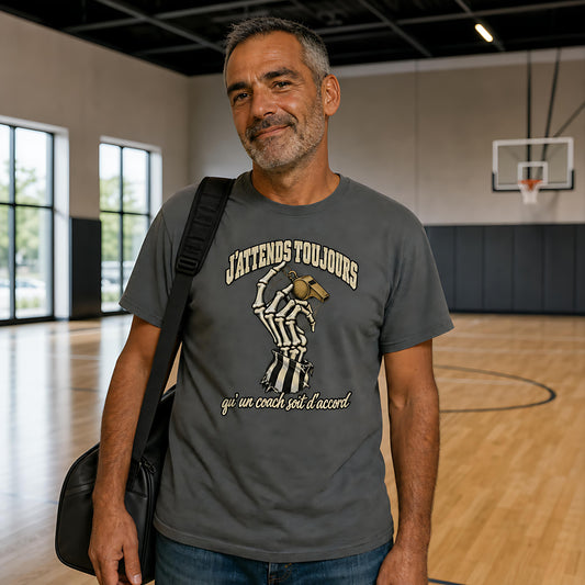 Arbitre portant le J'attends Toujours Tee coloris Pepper dans un gymnase lumineux, sac sur l'épaule, panier en arrière-plan – tee arbitre basket Halloween Ref' Crew