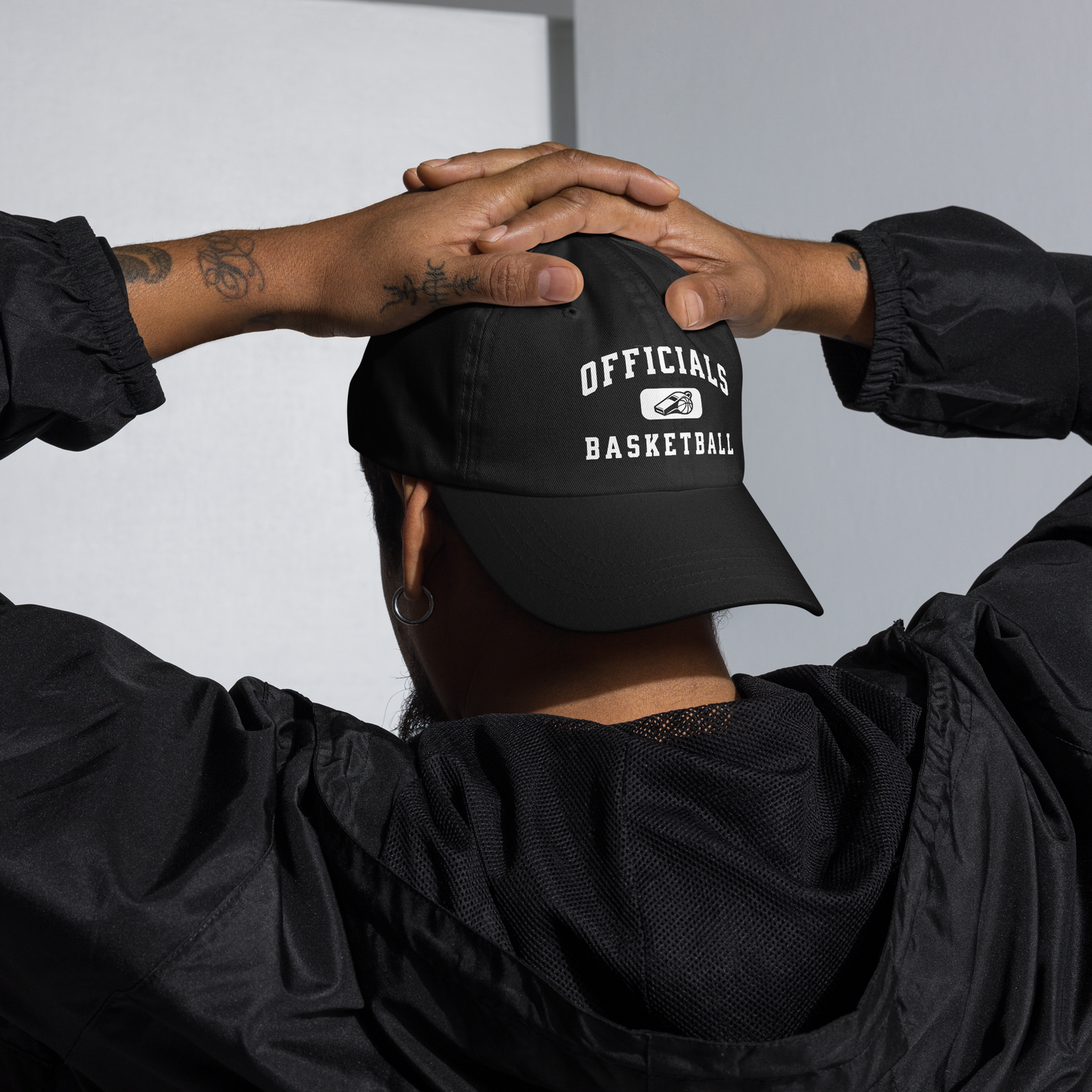 Black unstructured dad cap with "OFFICIALS BASKETBALL" text and whistle/ball logo, worn by a person.