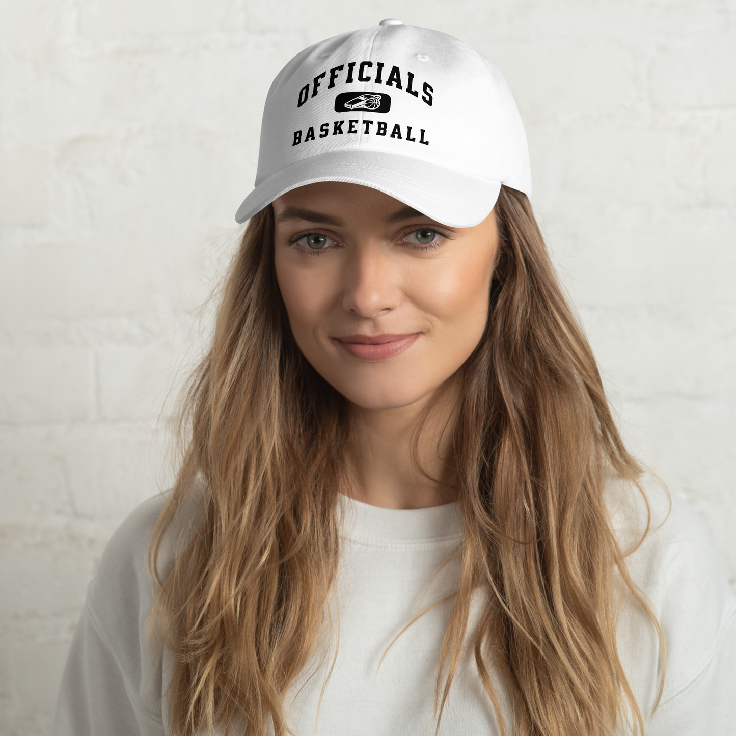 White Yupoong dad cap with "OFFICIALS BASKETBALL" text and whistle/basketball logo, worn by a woman.