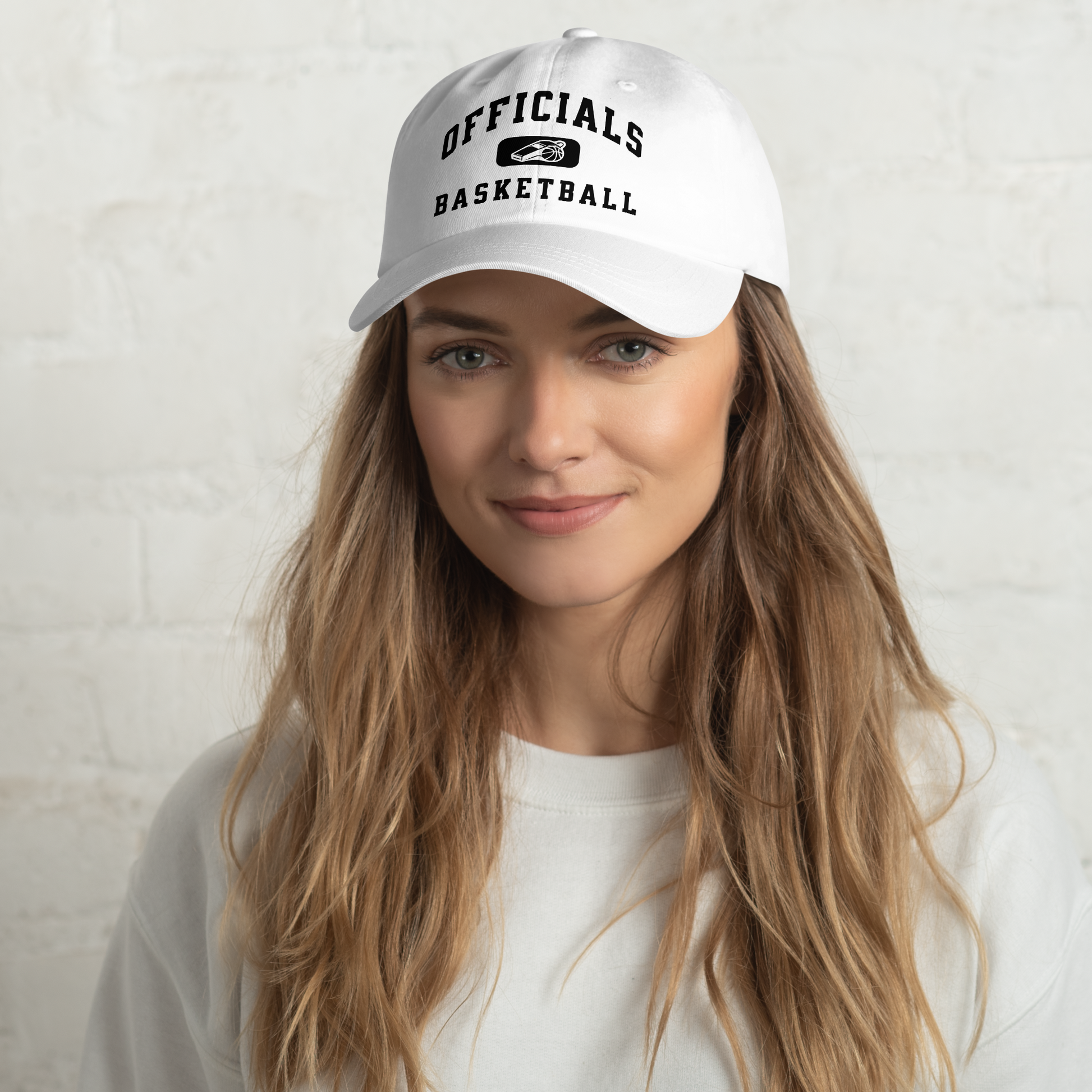 White Yupoong dad cap with "OFFICIALS BASKETBALL" text and whistle/basketball logo, worn by a woman.